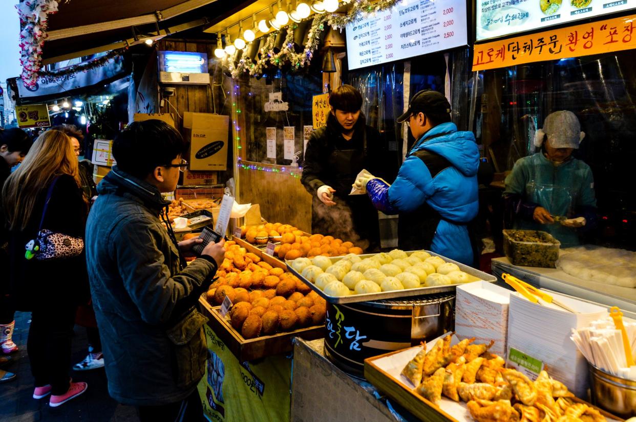 A Korean street food vendor at the Dongdaemun Market in Seoul, South Korea prepares, cooks, and serves food to eager customers. Photo taken during a cold winter day.