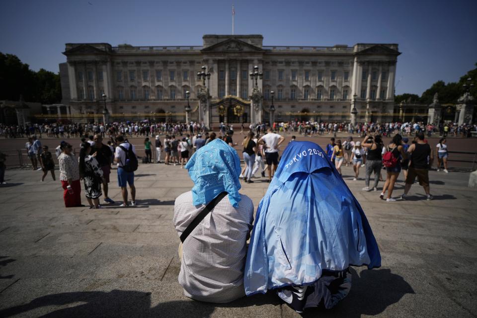 People sit covering their heads from the sun outside Buckingham Palace in London on Monday.  (Matt Dunham / AP)