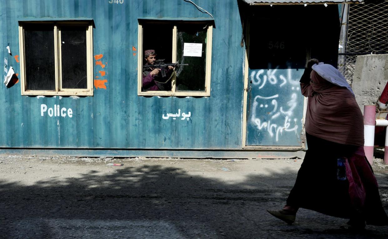 A Taliban fighter stands guard as a woman enters the government passport office, in Kabul, Afghanistan, in April 2022. (AP Photo/Ebrahim Noroozi)