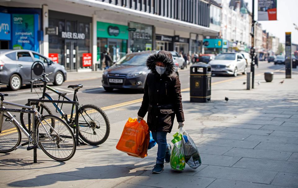 A woman wearing a protective face mask carries bags of shopping down a street in Wood Green in north London on March 27, 2020, after Britain's government ordered a lockdown to slow the spread of the novel coronavirus COVID-19. - Britain is under lockdown, it's population joining around 1.7 billion people around the globe ordered to stay indoors to curb the "accelerating" spread of the coronavirus. (Photo by Tolga AKMEN / AFP) (Photo by TOLGA AKMEN/AFP via Getty Images)