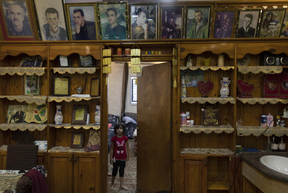 A Palestinian girl stands under framed portraits of family members, some of them were killed by the Israeli army according to Bahjat al-Alami, the grandfather of slain Mohammed al-Alami, 12, at the family house, in the West Bank village of Beit Ummar, near Hebron, Wednesday, Aug. 4, 2021. (AP Photo/Nasser Nasser)