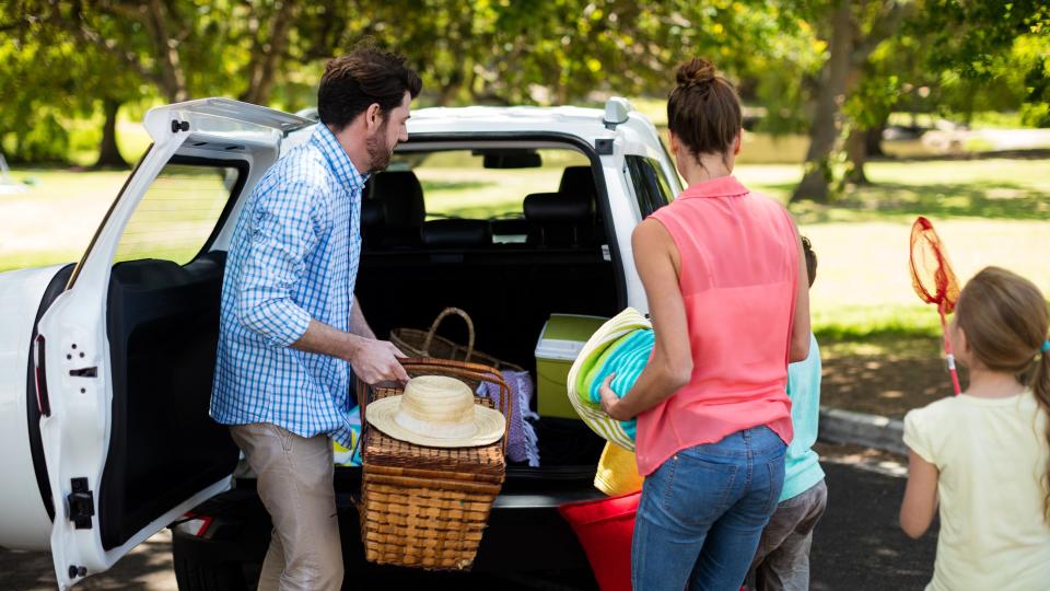 Family placing picnic items in car trunk at park.