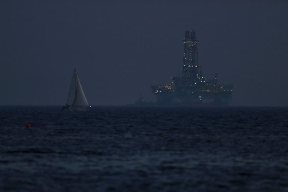 An offshore drilling rig is seen in the waters off Cyprus' coastal city of Limassol as a sailboat sails in the foreground on Sunday, July 5, 2020. Cyprus has in recent years been a resupply stop for rigs drilling in the eastern Mediterranean, including waters were the Cypriot government has licensed international energy companies to search of hydrocarbons. (AP Photo/Petros Karadjias)