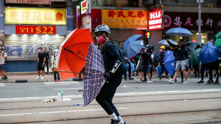 Ein Demonstrant mit Regenschirmen nimmt an einem Protestmarsch teil. Foto: dpa