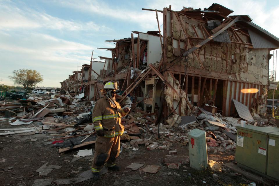 Fire personnel from other areas walk among the remains of an apartment complex next to the fertilizer plant the day after the blast.