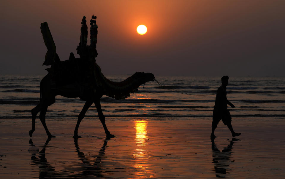 A Pakistani man and his camel are silhouetted, against the last sunset of 2023 at Clifton beach in Karachi, Pakistan, Sunday, Dec. 31, 2023. (AP Photo/Fareed Khan)