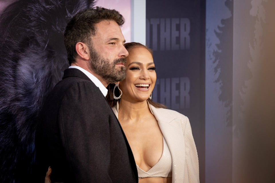 Ben Affleck and Jennifer Lopez at a red carpet event. Jennifer wears a crop top with a blazer, while Ben is in a suit