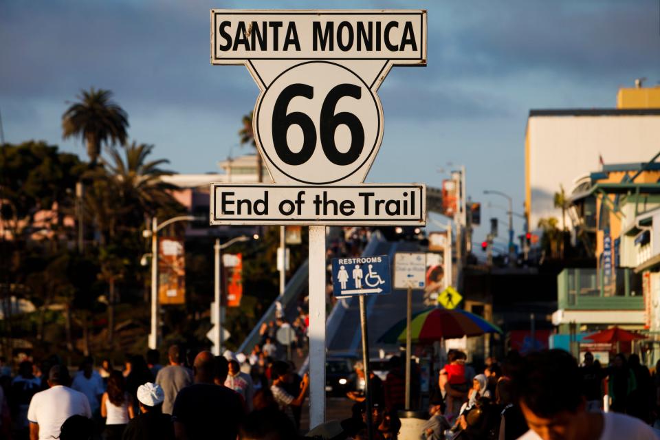 Pedestrians walk past a sign for the end of the historic Route 66 Highway at the Santa Monica Pier in Santa Monica, California, U.S., on Monday, Aug. 5, 2013.