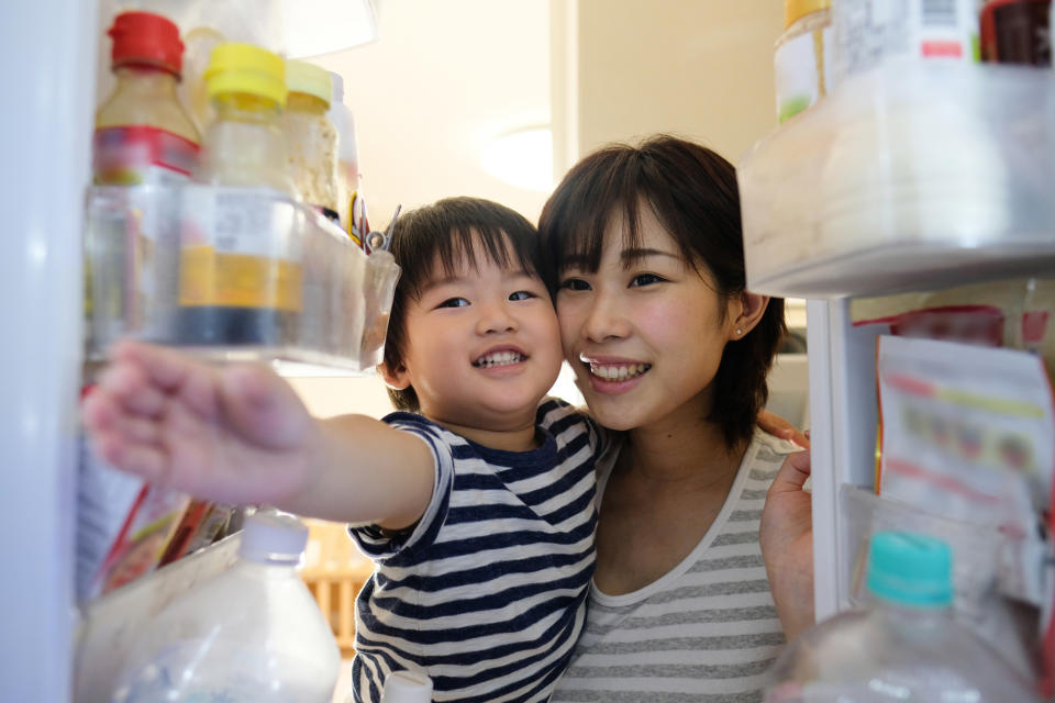 Homemaker opening door of refrigerator with toddler in her arms