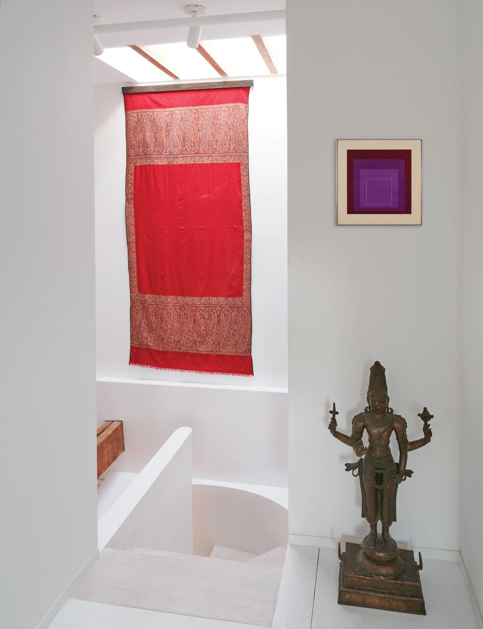 An antique pashmina shawl hangs in the stairwell. A bronze Vishnu sculpture stands under a Josef Albers artwork.