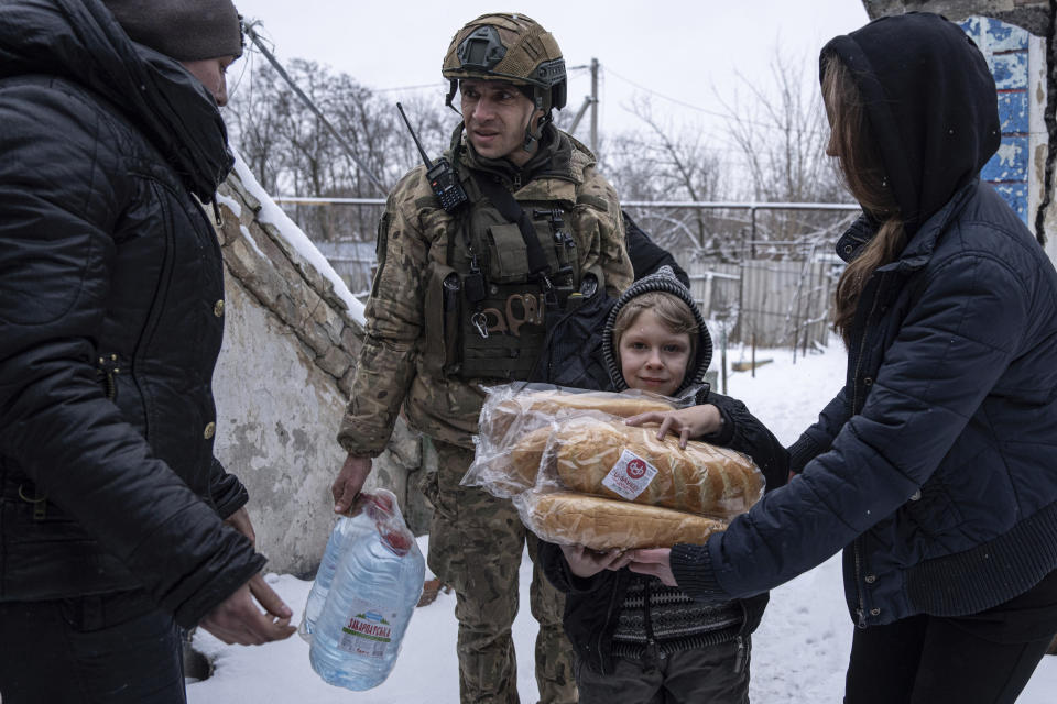 A Ukrainian police officer of the White Angels unit distributes humanitarian aid to a family in Krasnohorivka, Ukraine, Friday, Feb. 17, 2023. A special unit known as the White Angels risk their lives to head into front-line villages and towns, knocking on doors and pleading with the few remaining residents to evacuate. (AP Photo/Evgeniy Maloletka)