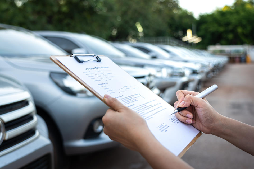 Action of a customer is signing on the agreement term of car rental service. Close-up and selective focus a human's hand with blurred background of cars in row. Business and transportation concept.