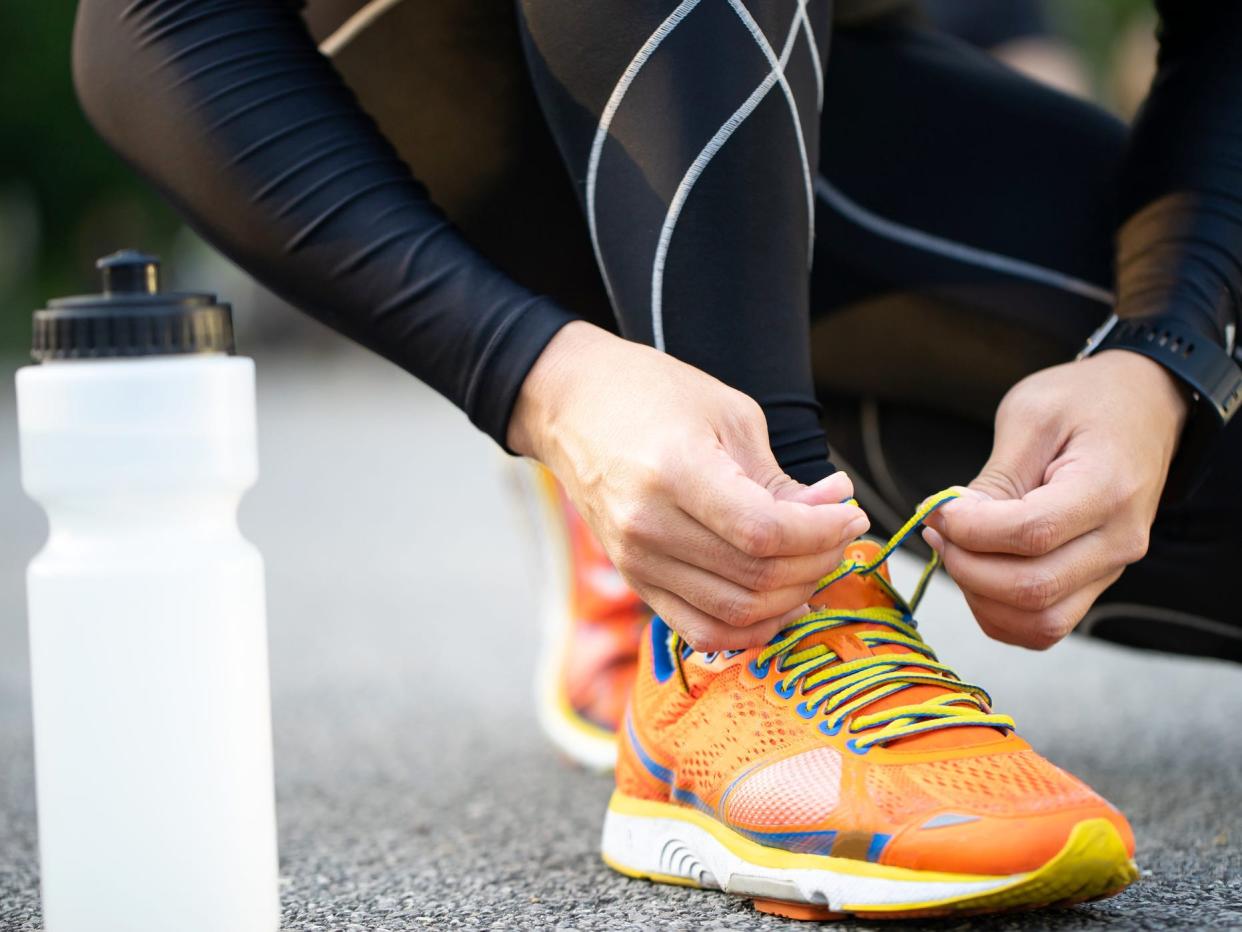 a close up of a runner in workout tights tying shoes next to a water bottle on the pavement