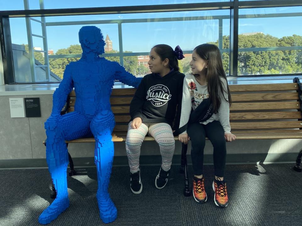 A Lego man in blue sits with visitors at the California Science Center's "The Art of the Brick."