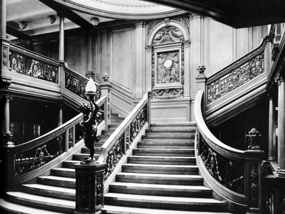 A black-and-white image of the grand, curving staircase on the Titanic that is illuminated by the skylight above.