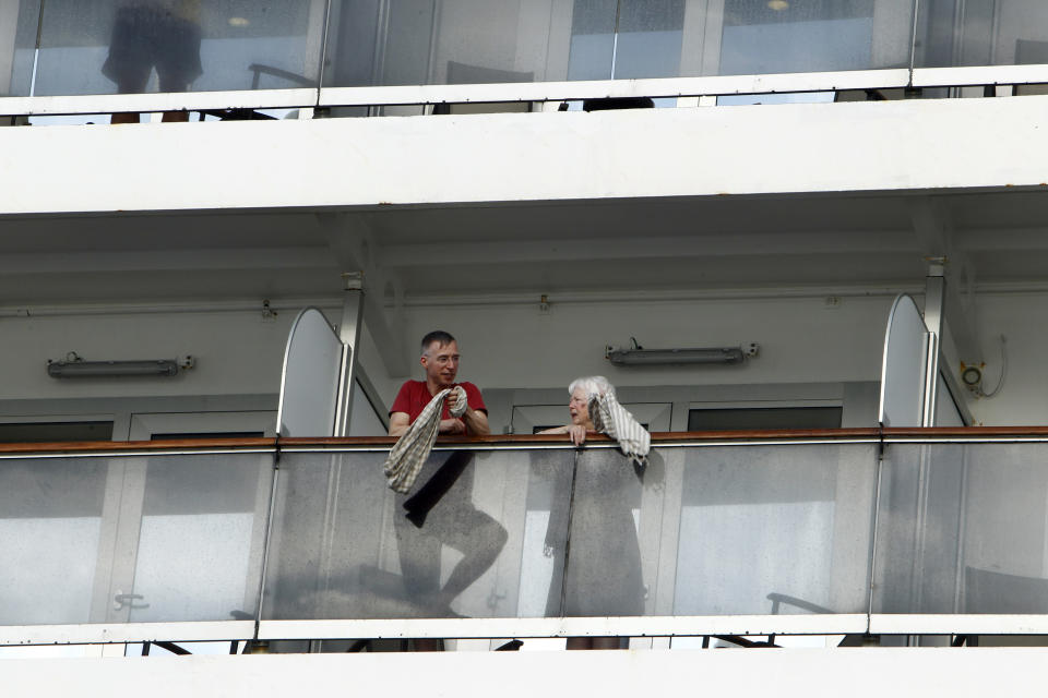 Passengers talk at each other on the MS Westerdam, owned by Holland America Line, docked at the port of Sihanoukville, Cambodia, Friday, Feb. 14, 2020. Hundreds of cruise ship passengers long stranded at sea by virus fears cheered as they finally disembarked Friday and were welcomed to Cambodia. (AP Photo/Heng Sinith)