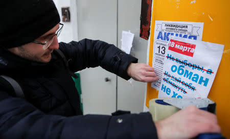 An activist and supporter of Russian opposition leader Alexei Navalny puts up a flier promoting a boycott of the upcoming presidential election near the entrance to a block of flats in Moscow, Russia February 10, 2018. Picture taken February 10, 2018. The flier reads "March 18. Not election but deceit. Don't let yourself be deceived. Don't go." REUTERS/Maxim Shemetov