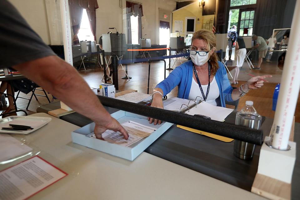 Volunteer Kelly Grech slides a ballot underneath a plastic partition to protect her from transmission of COVID-19 while helping out at town election on Saturday, June 27, 2020. Normally there would be two volunteers to check in residents but the town clerk applied for a waiver with the Secretary of State to reduce the number of poll workers at town election.