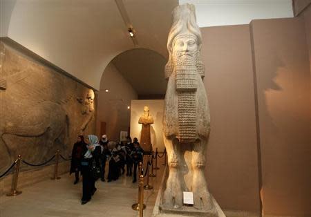 Visitors walk past ancient Assyrian human-headed winged bull statues at the Iraqi National museum in Baghdad December 31, 2013. REUTERS/Ahmed Saad