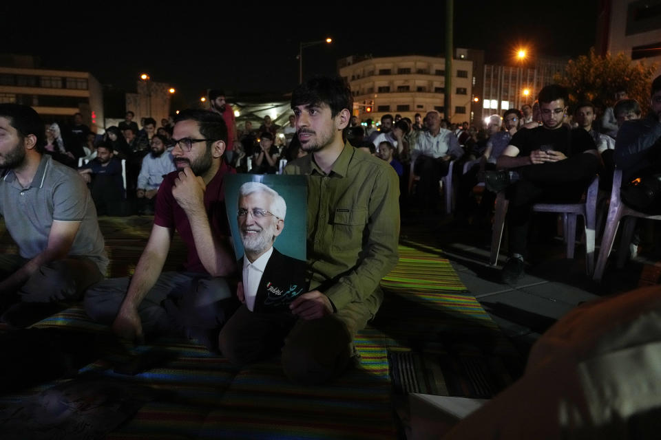 A supporter of candidate Saeed Jalili, holds his poster during a public viewing of a candidate debate for the June 28 presidential election on a giant screen in downtown Tehran, Iran, Monday, June 17, 2024. The election comes at a time of heightened tensions between Iran and the West over its arming of Russia in that country's war on Ukraine. (AP Photo/Vahid Salemi)