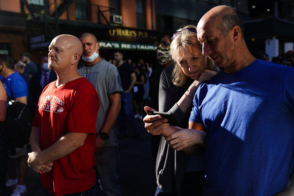 A couple gathers with others outside the National September 11 Memorial and Museum as they view on their smartphone a ceremony marking the 20th anniversary of the 9/11 terrorist attacks, Saturday, Sept. 11, 2021, in New York. (AP Photo/Matt Rourke)