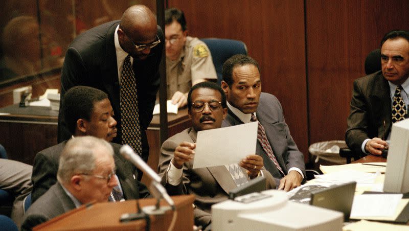 With defendant O.J. Simpson, far right, looking on, lead defense team attorney Johnnie L. Cochran Jr., second from right, examines a pictures of Simpson’s next door neighbor Wolfgang Salinger’s estate, March 3, 1995, in a Los Angeles courtroom.