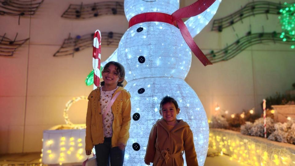 Yvette and Lynette Guillen stand with a snowman Thursday night at the Amarillo Botanical Gardens during its Christmas in the Garden event.