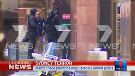 A man (2nd L in blue jacket), surrounded by armed police, gestures towards a door where he had just ran out of, outside the Lindt cafe, where hostages are being held, in this still image taken from video from Australia's Seven Network on December 15, 2014. REUTERS/Reuters TV via Seven Network