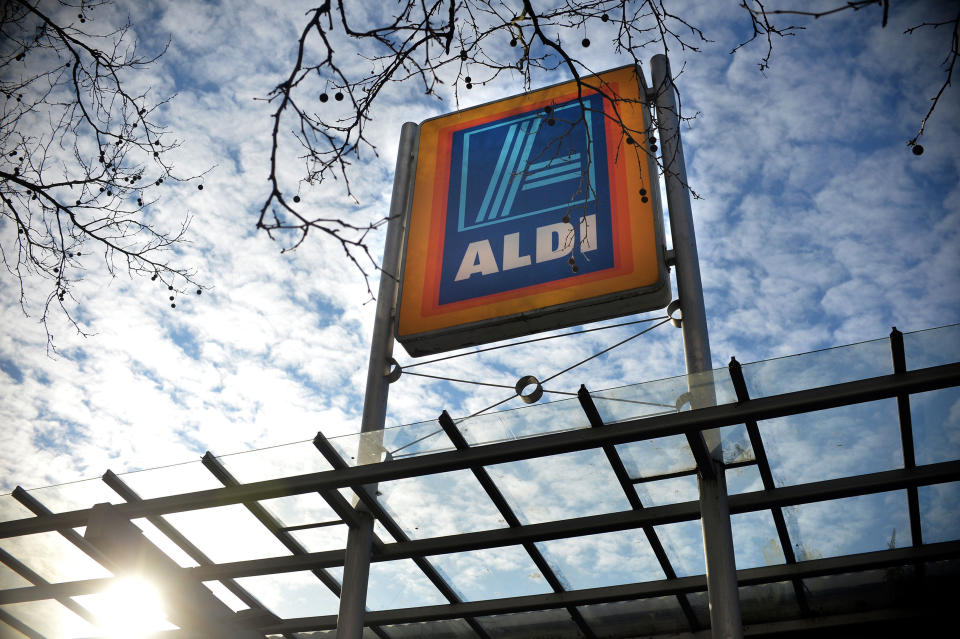 Aldi sign on a supermarket roof with blue sky and clouds over head.