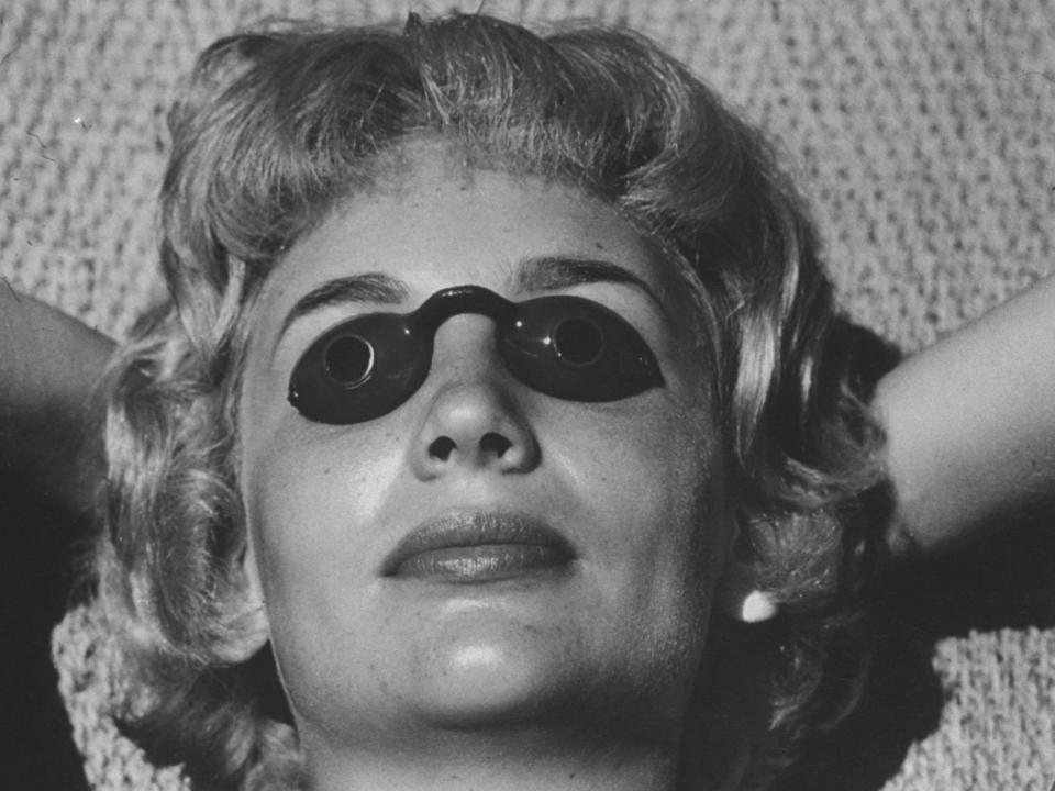 A woman tans with small eye protectors covering her eyes.