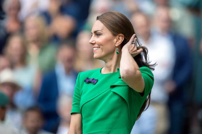 Woman in an elegant green dress with a bow pin, touching her hair, at an outdoor event