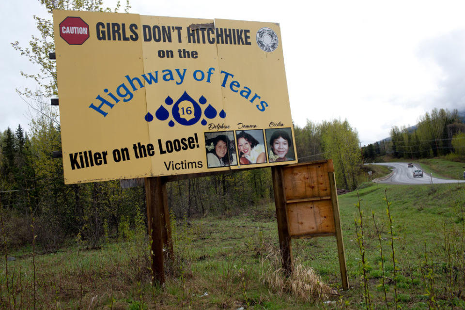 Cars drive past a road sign on Canada's Route 16 that says girls don't hitchihike on the highway of tears, killer on the loose