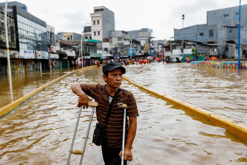 A man uses crutches to walk through floodwaters at the Jatinegara area after heavy rains in Jakarta