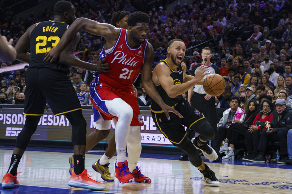 Golden State Warriors' Stephen Curry, right, drives to the basket against Philadelphia 76ers' Joel Embiid, center, during the first half of an NBA basketball game, Saturday, Dec. 11, 2021, in Philadelphia. (AP Photo/Chris Szagola)