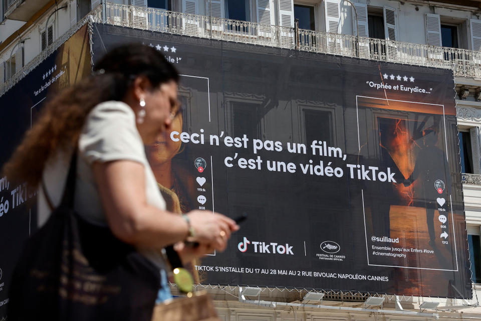 The 75th Cannes Film Festival - Cannes, France, May 20, 2022. A woman looks at her mobile phone as she walks past an advertising poster for TikTok app displayed on the Croisette during the film festival. REUTERS/Sarah Meyssonnier