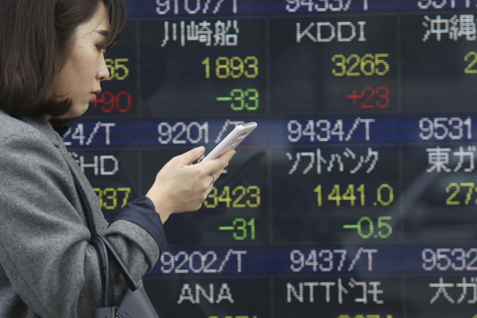 In this Wednesday, Dec. 18, 2019, photo, a woman walks by an electronic stock board of a securities firm in Tokyo. Stocks were mixed in early trading in Asia on Friday after Wall Street posted more record highs, extending the market's gains for the week. (AP Photo/Koji Sasahara)