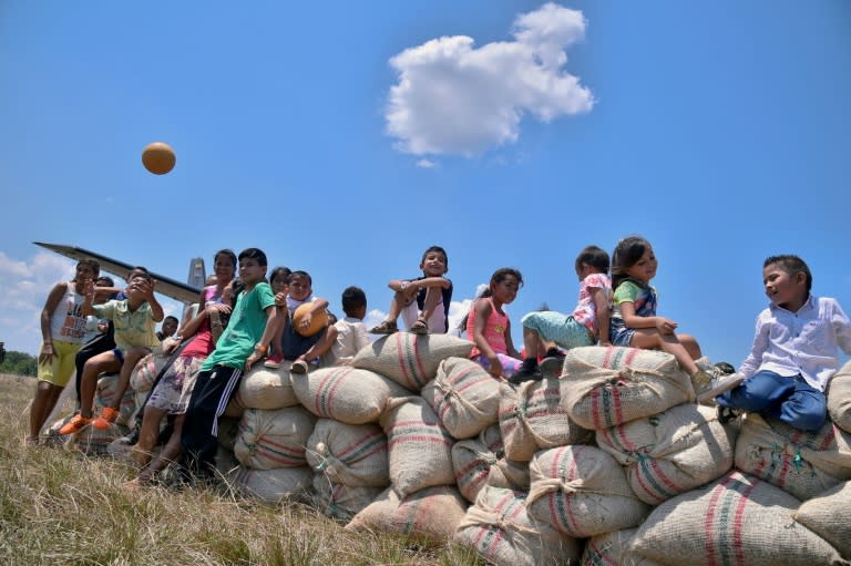 Children sit on sacks of cocoa beans set to be loaded onto a Colombian Air Force plane at the Guerima village airstrip in the municipality of Cumaribo, Vichada department, eastern Colombia, on February 16, 2017