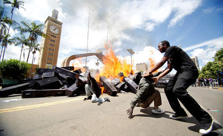 FILE PHOTO: Kenyan social-political activist Boniface Mwangi (R) reacts as mock coffins burn outside the Kenyan parliament during a protest dubbed "State Burial-Ballot Revolution", a demonstration against legislators plan to receive higher bonuses, in the capital Nairobi, January 16, 2013. REUTERS/Thomas Mukoya/File Photo