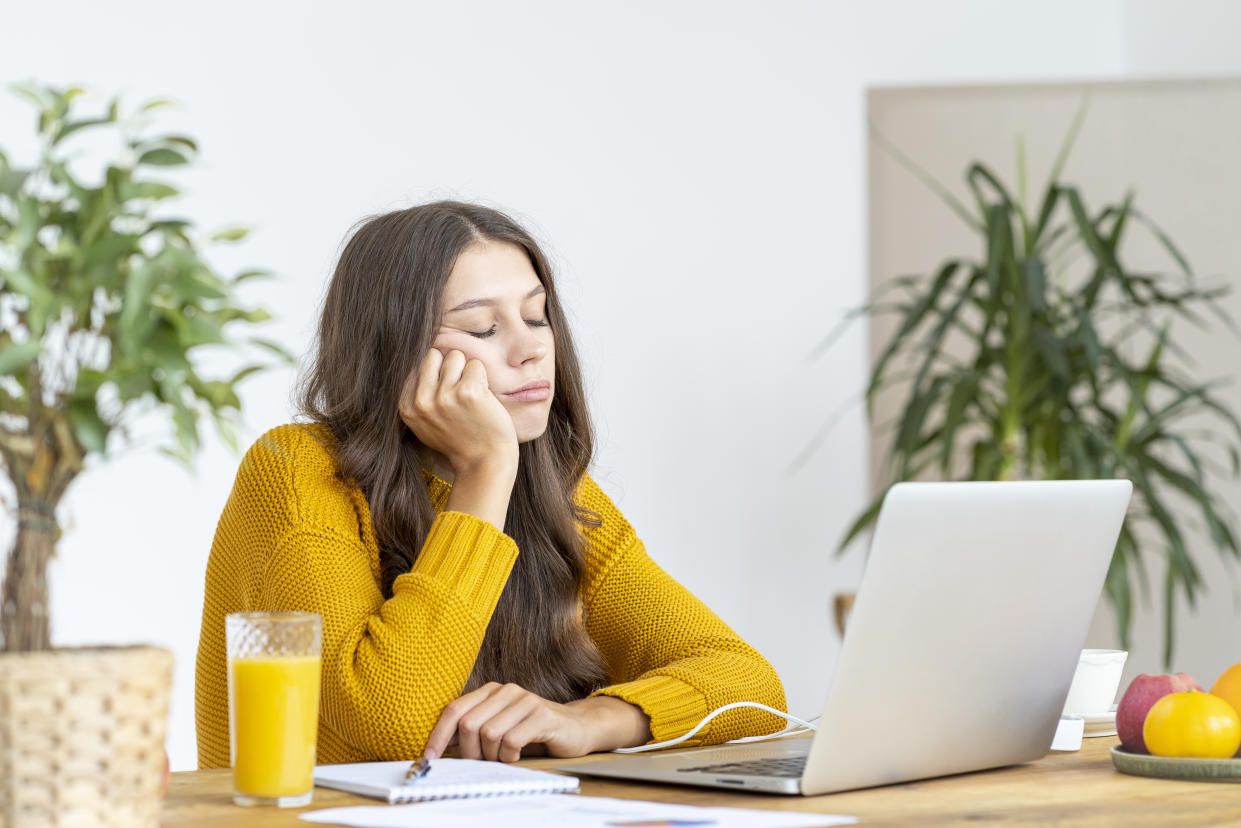 Young girl fell asleep in front of laptop. Cute woman is bored, tired or overworked. Cozy home environment. Pretty female in bright yellow jumper working on laptop at home