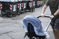 A man pushes a baby stroller past a wild boar sniffing past trash bins in Rome, Friday, Sept. 24, 2021. They have become a daily sight in Rome, families of wild boars trotting down the city streets, sticking their snouts in the garbage looking for food. Rome's overflowing rubbish bins have been a magnet for the families of boars who emerge from the extensive parks surrounding the city to roam the streets scavenging for food. (AP Photo/Gregorio Borgia)