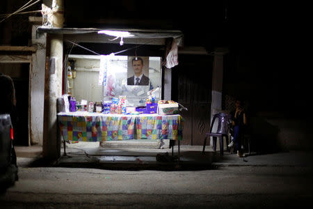 A man sells chocolates and biscuits, as a poster depicting Syria's President Bashar al-Assad is seen in the background, in Deir al-Zor, Syria September 20, 2017. Picture taken September 20, 2017. REUTERS/Omar Sanadiki