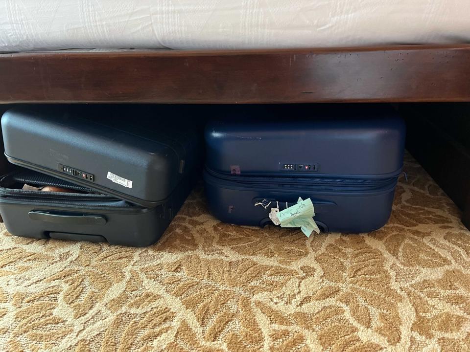 Two suitcases stored underneath a bed on carpeting.