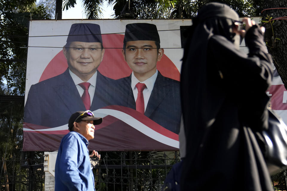 Protesters walk past the election banner of presidential frontrunner Prabowo Subianto, left, and his running mate Gibran Rakabuming Raka, the eldest son of Indonesian President Joko Widodo, as they arrive for a rally alleging a widespread fraud in the Feb. 14 presidential election, near the General Election Commission's office in Jakarta, Indonesia, Wednesday, March 20, 2024. Subianto, a former general linked to past human rights abuses who had the incumbent President Joko Widodo's tacit backing is currently leading the tally with nearly 60% of the votes. (AP Photo/Dita Alangkara)