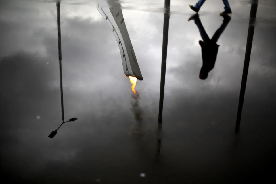 The Olympic flame is reflected in a puddle while lit during a test in the Olympic Park for the upcoming 2014 Winter Olympics as a pedestrian passes by, Friday, Jan. 31, 2014, in Sochi, Russia. (AP Photo/David Goldman)