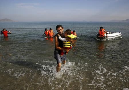 An Iranian migrant cries as while carrying his son after a small group of exhausted migrants from Iran arrived by paddling an engineless dinghy from the Turkish coast (seen in the background) at a beach on the Greek island of Kos August 15, 2015. REUTERS/Yannis Behrakis