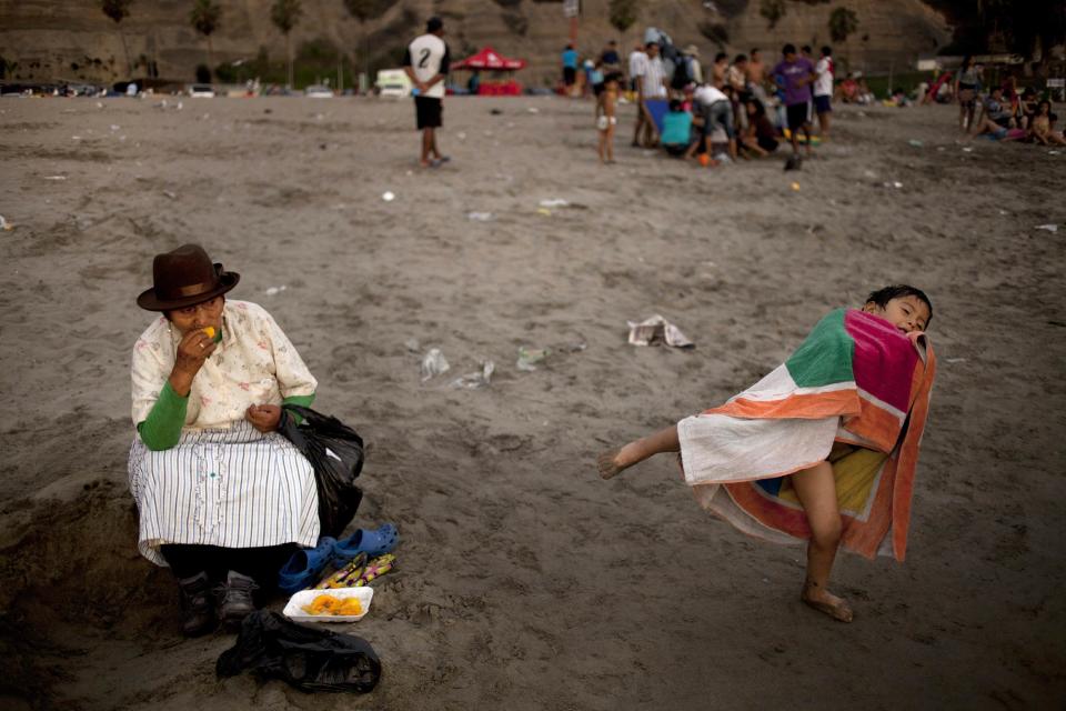 In this Jan. 18, 2013 photo, a woman snacks on mango fruit as her grandson plays nearby on Agua Dulce beach in Lima, Peru. While Lima's elite spends its summer weekends in gate beach enclaves south of the Peruvian capital, the working class jams by the thousands on a single municipal beach of grayish-brown sands and gentle waves. On some weekends during the Southern Hemisphere summer, which runs from December until March, as many as 40,000 people a day visit the half-mile-long (kilometer-long) strip of Agua Dulce. (AP Photo/Rodrigo Abd)