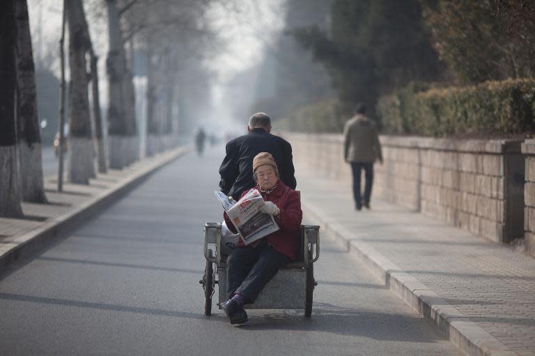 An elderly woman reads a newspaper as she rides on the back of a tricycle in Beijing on March 8, 2013