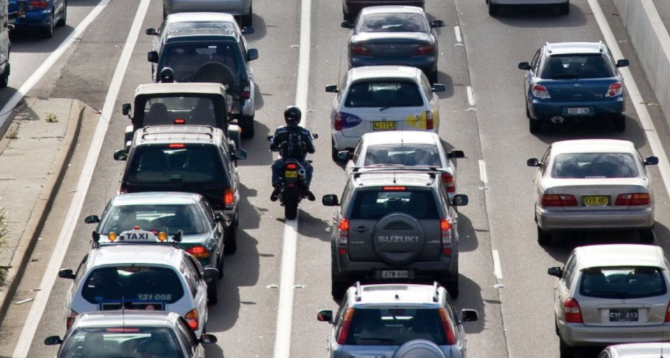 Motorbike travels down the middle of a lane in busy traffic.