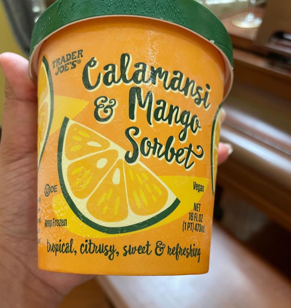 Hand holding a tub of Trader Joe's Calamansi & Mango Sorbet labeled as vegan, tropical, citrusy, sweet & refreshing