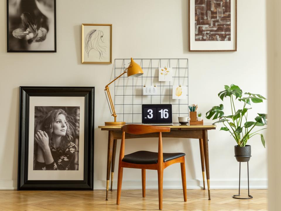 Wooden chair at desk with yellow lamp and laptop in home office interior with gallery.